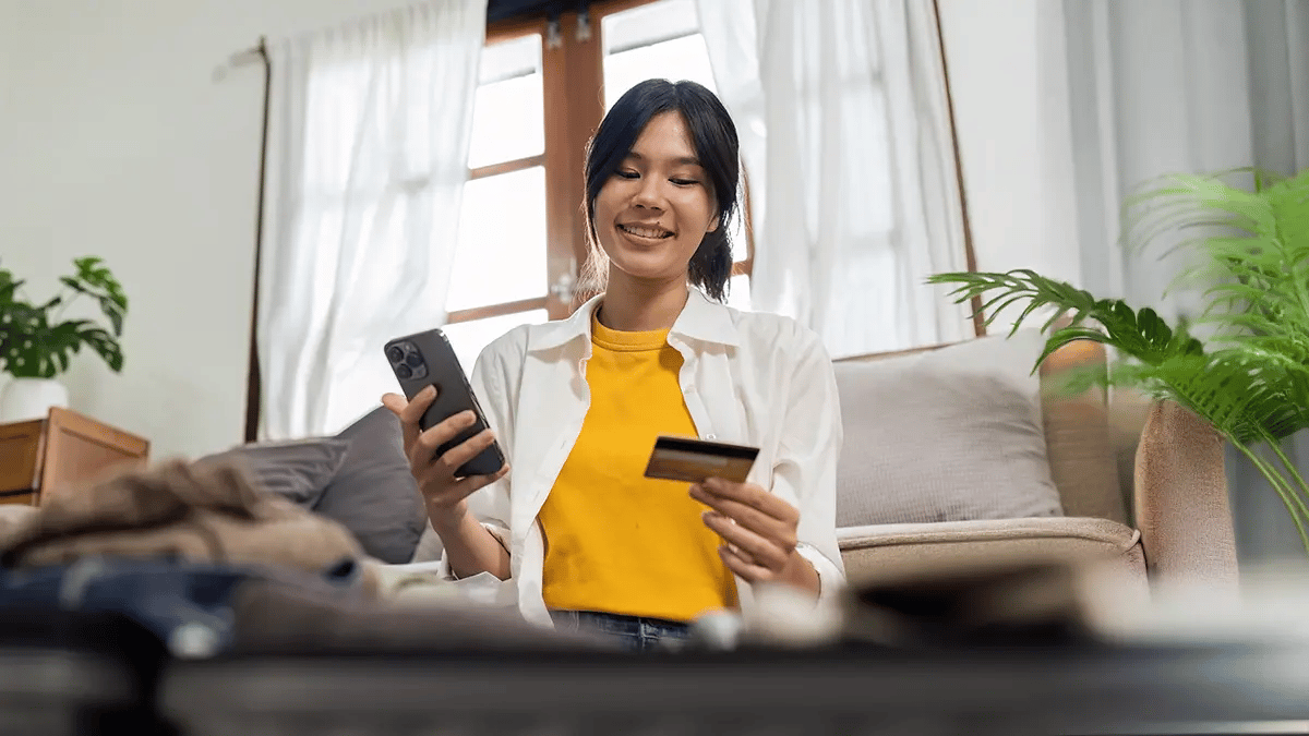 Woman holding a credit card and a phone, with a suitcase blurred in the foreground.