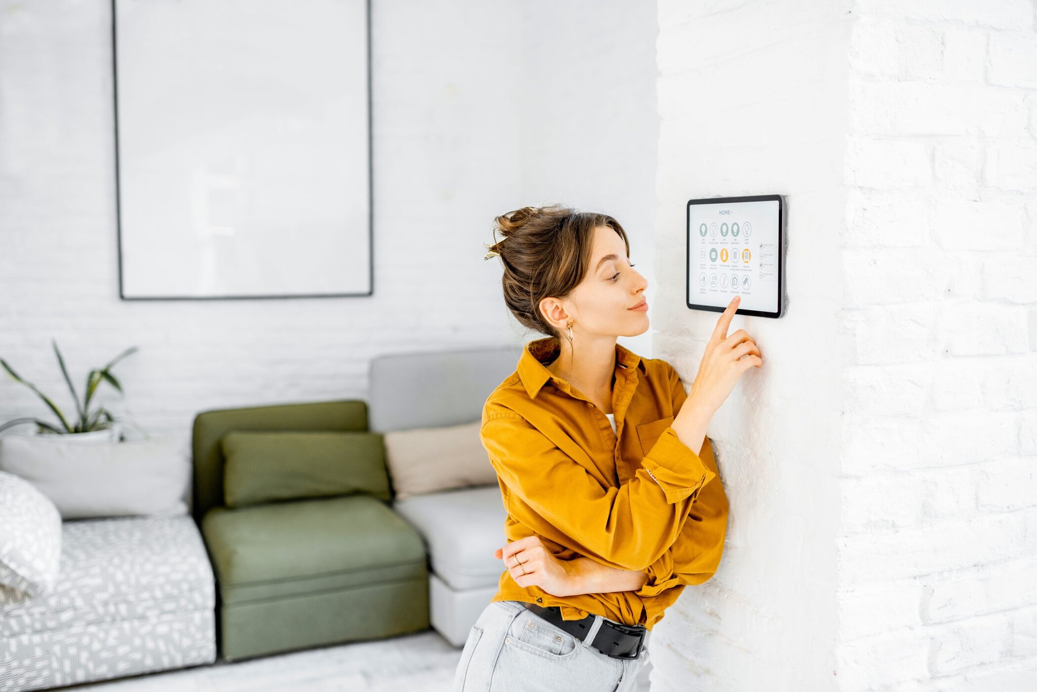 Woman controlling home with a digital touch screen panel installed on the wall in the living room, hotel trends, digitalisierung, smart rooms